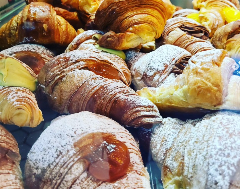 Cornetti sfogliati con zucchero a velo e ripieni di pistacchio, cioccolato, crema e confettura in una vetrina