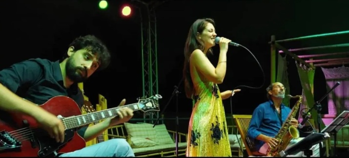 Cantante in abito giallo a fiori affiancata da chitarra rossa e sassofono sulla terrazza serale del Casita Bar